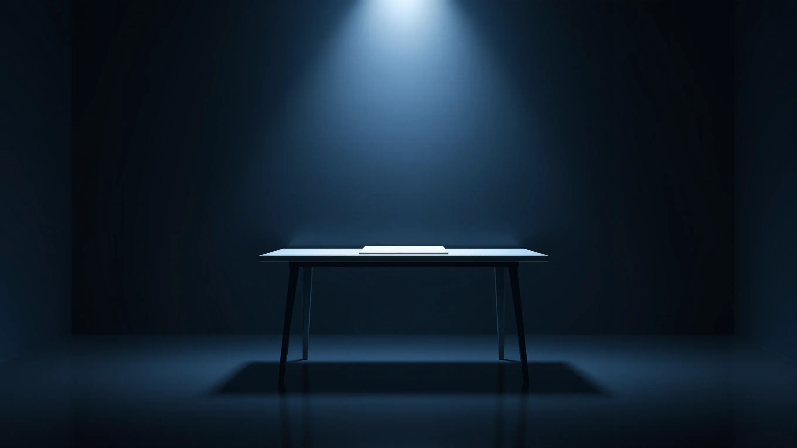 O masă goală într-o cameră întunecată, cu o singură foaie albă sub un con de lumină